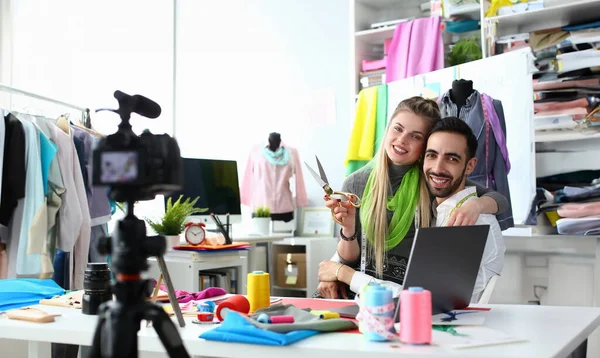 Fashion Industry Blog Content Clothes Creation. Blond Seamstress with Scissors and Handsome Caucasian Designer Hugging at Wokplace. Happy Sewing Production Team Recording Vlog at Camera
