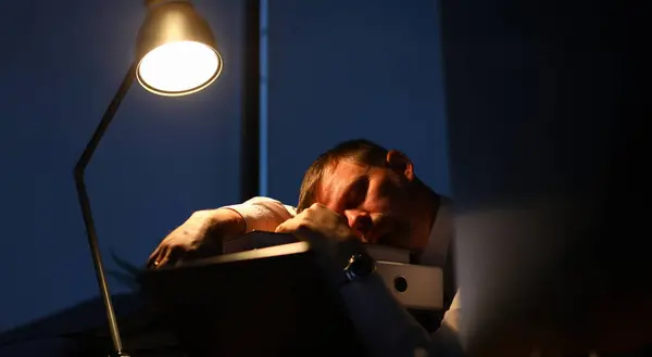 Businessman sleeping on office table evening time background. Man wants to go home and lives at work. Overtime night work concept.