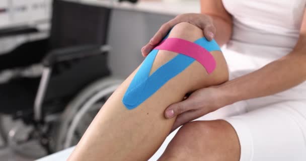 女は彼女の痛み膝を手で持っていますとともにKinesioテープ4K映画スローモーション 外傷後の運動療法リハビリテーションの概念 — ストック動画