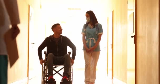 Νοσοκόμα Που Περπατάει Ασθενή Αναπηρικό Καροτσάκι Στο Διάδρομο Και Χαιρετάει — Αρχείο Βίντεο