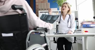 Doktor tekerlekli sandalyedeki kadına röntgen görüntüsü gösteriyor. Engelliler için rehabilitasyon kliniği ve tedavi