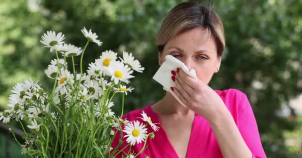 アレルギー症状を持つ若い女性は カモミールの花の花束を保持公園に立っている間 鼻を吹く 病気の女の子はくしゃみと花粉症のために組織に彼女の鼻を吹く — ストック動画