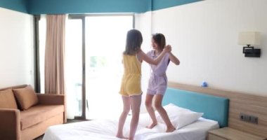 Eğlenen iki küçük kız kardeş yatak odasında yatağa atlıyor. Mutlu çocuklar evde birlikte zıplıyorlar.