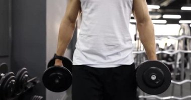 Spor salonunda dambıllarla yürüyen bir sporcu. Beden eğitiminde kuvvet.