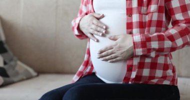 Hamile kadın göbeğine şefkatle dokunuyor. Çocuk konseptinin doğmasını beklemek