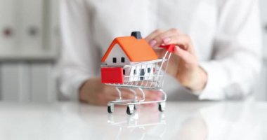 Alışveriş arabasındaki klasik ev modeli emlakçı tarafından taşınıyor. Kredi konseptiyle ev almak