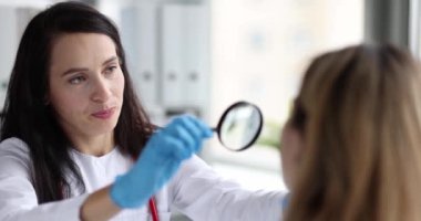 Kadın doktor hasta yüzünün derisini büyüteç 4K film yavaş çekim kullanarak inceliyor. Dermatoloji kavramı