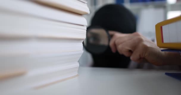 虫眼鏡のバラクラバの人は事務所の書類を見ています 産業用スパイと知的財産窃盗の概念 — ストック動画