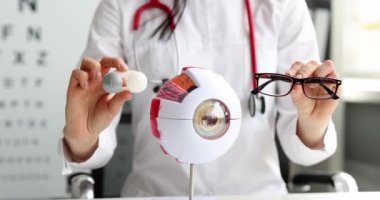 Doktor göz doktoru, kontakt lens ve gözlüklü konteynırı yapay insan gözü modeli 4K film ağır çekimin önünde tutuyor. Miyop kavramının düzeltilmesi