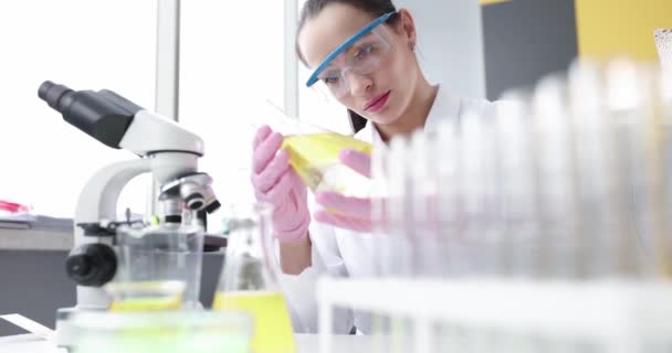 Mujer Química Examinando Líquido Amarillo Frasco Delante Del Microscopio Laboratorio — Vídeos de Stock
