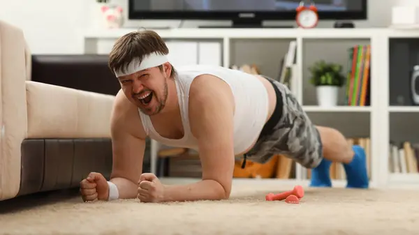 Young attractive fitness man lies on a fat mat with overweight performs stretching exercises and smiles