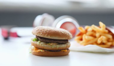 Hamburger ve kızarmış patates kulaklık ile masaüstü ofis öğle yemeği molası gıda teslim kavramı sırasında lay