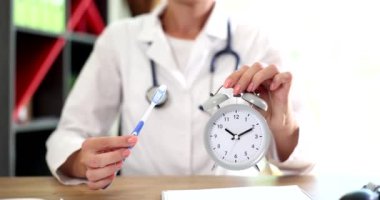 Doctor dentist holds toothbrush and an alarm clock in hands. Time to brush your teeth and dental care and personal hygiene concept