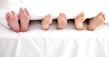 Legs of woman with two men in bed in bedroom. Polygamy in men and women