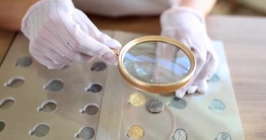 Numismatics and old collectible silver coins. Collector with magnifying glass in gloves holds ancient coin