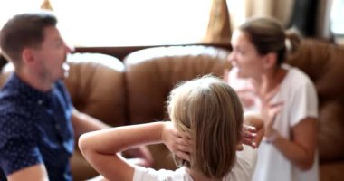 Rear view of child girl covers ears with hands while parents are quarreling. Child suffering from parental quarrels neglect or divorce