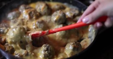 Cook stirs meatballs in creamy sauce in pan. Meatballs at home