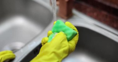 Hand in yellow glove squeezes a washcloth with detergent closeup. Detergent for dishes
