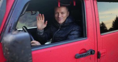 Smiling male SUV driver waving hand in greeting. Offroad adventure hunters