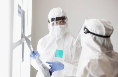 Koruyucu giysili ve gözlüklü iki doktor hastanın röntgenini tartışıyor. Coronavirüs enfeksiyonu konsepti yüzünden çok hasta.