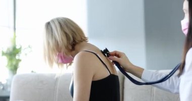 Doktor, koruyucu maskeli bir kadının ciğerlerindeki hırıltıyı dinliyor. Zatürree ve bronşit tedavisi kavramı