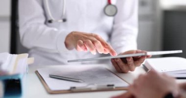 Doktor hastayla randevuda tabletle çalışır. Beyaz üniformalı GP doktoru hasta teşhisinin sonuçlarını tablet ekrandaki hastaya danışırken tartışır.