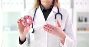 Doktor diyetisyen, sevimli pembe çörekleri yakın çekim 4K filmi yavaş çekimde gösteriyor. Beslenme konseptinde abur cubur fazla karbonhidrat