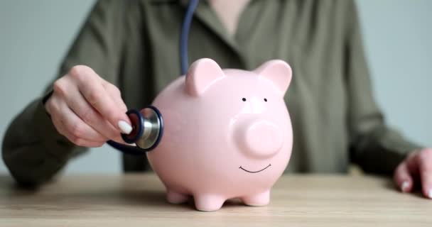 Woman Hand Applying Stethoscope Pink Piggy Bank Coins Closeup Movie — Stock Video