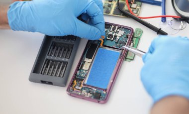 Close-up of technician fixing broken mobile phone, set new battery and cover, return old cellphone to life. Workplace with instruments. Handyman concept