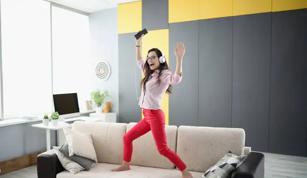 Portrait of happy woman dancing on couch, listen to music in headset and sing. Happy mood, good news, celebrate, party. Positivity, fun, go nuts concept