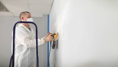 Portrait of male worker in protective costume polish wall with special equipment. Sander machine in work. Renovation, construction, interior design concept