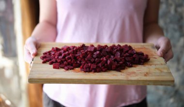 Kadın tahtanın üzerinde doğranmış pancar kökü tutuyor. Vejetaryen yemekleri pişirmek ve pancar konseptinin faydaları