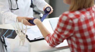 Close-up of physiotherapist man put bandage on female patient hand, post traumatic rehabilitation. Medicine, healthcare, recovery, hospital help concept