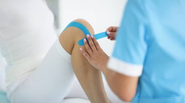 Fizyoterapistin yakın çekimi hastaların dizlerine kinezyoloji bandı yapıştırdı. Ağrıyı, rehabilitasyon merkezini, masaj dolabını kaldırdı. Fizik tedavi, iyileşme konsepti
