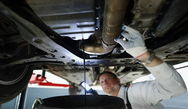 Portrait of mechanic man change oil under auto, car maintenance service, oil dripping. Qualified worker fix your vehicle. Pit stop, repair, service concept