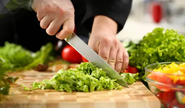 Cook holds knife in hand and cuts on cutting board green for salad or fresh vegetable soup with vitamins. Raw food and vegetarian recipe book in modern society popular concept.