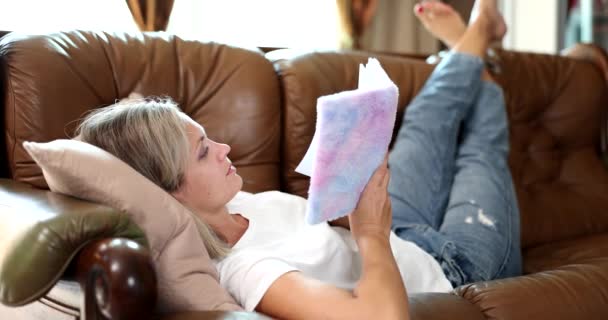 年轻女人躺在沙发上看侦探小说 教育书籍和家庭爱好 — 图库视频影像