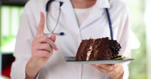 チョコレートケーキと親指を持っている医師の手は注意ジェスチャーを持ちます お菓子や食事の利点と害 — ストック動画