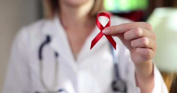 医師はエイズやHivから人々を守るための国際デーの赤いリボンのシンボルを手に持っています 獲得免疫不全症候群の発症による免疫系への損傷 — ストック動画