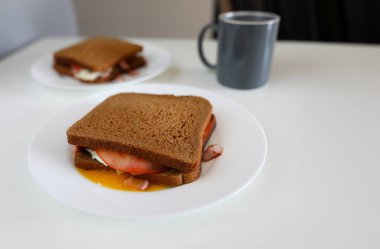 Tabakta sosisli siyah sandviç var. Soslu basit kahvaltı ekmeği. Yemek pişirmede yeni yetenekler kazanıyorsun. Masada, evde pişmiş tam tahıllı sandviç var. Lezzetli yemekler.