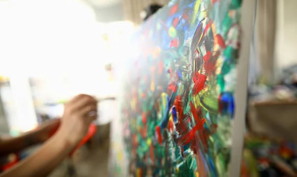 Man paints large bright abstract painting picture. Hands hold brush with multi-colored paint. Learning technique in an art workshop. Classic drawing lessons. Color strokes are painted natural canvas