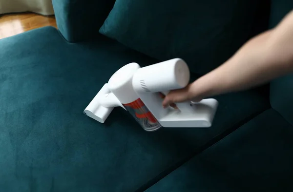 Hand vacuums upholstered furniture in apartment. Design features and unique advantages household appliances for dry cleaning in apartment. Tool sucks in dust and small debris on couch