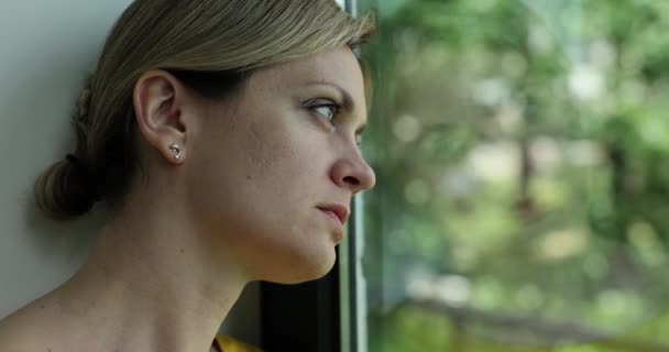 独自在家的年轻女子想到孤独或悲伤 坐在窗前 带着寂寞的表情望着外面的街道 抑郁和压力 — 图库视频影像