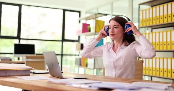 ビジネスの女性はヘッドフォンでテーブルに座り 音楽を聴き オフィスで仕事をしています マネージャは クライアント教育のウェビナーと距離オンラインクラスの概念を助言 — ストック動画