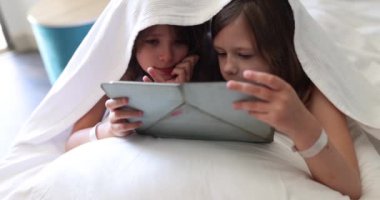 Dijital tabletle battaniyenin altında iki kız çocuğu. Çocukluk rüyası çevrimiçi video oyunu konsepti