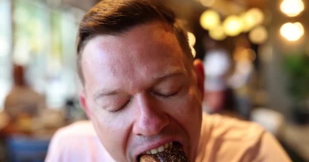 カフェでおいしいドーナツパンをかむ幸せな男 昼休みを楽しむ男 甘いパン — ストック動画