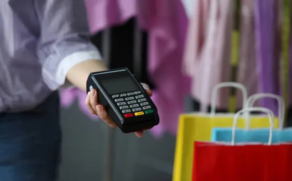 Hand holds out terminal for credit card payment. Simple and easy to manage finances on credit card. Purchase clothes during fall. Portable terminal for credit card payment. Mobile terminal