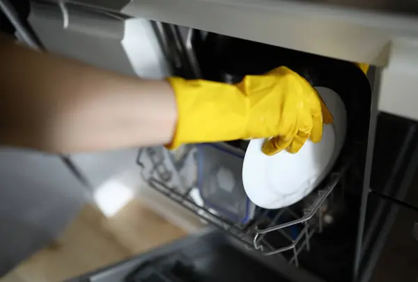 Hands in gloves put plate to dishes in dishwasher. Features washing dishes in an automated way. Use dishwashers in apartment. Equipment high-quality dishwashing does not require lot time