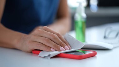 Bir kadın antiseptik peçeteyle cep telefonu ekranını siliyor. Covid-19 salgını sırasında hijyenik davranış standartları