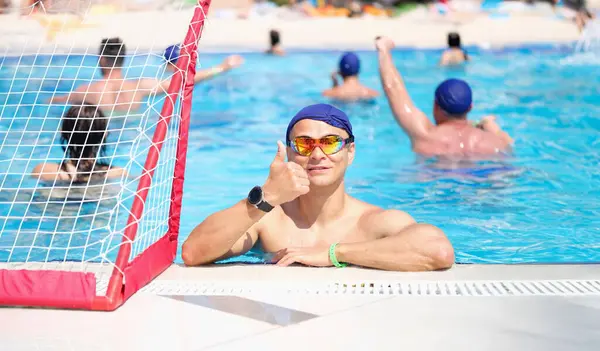 Young man in swimming goggles and caps showing thumb up in pool. Quality sports training on water concept